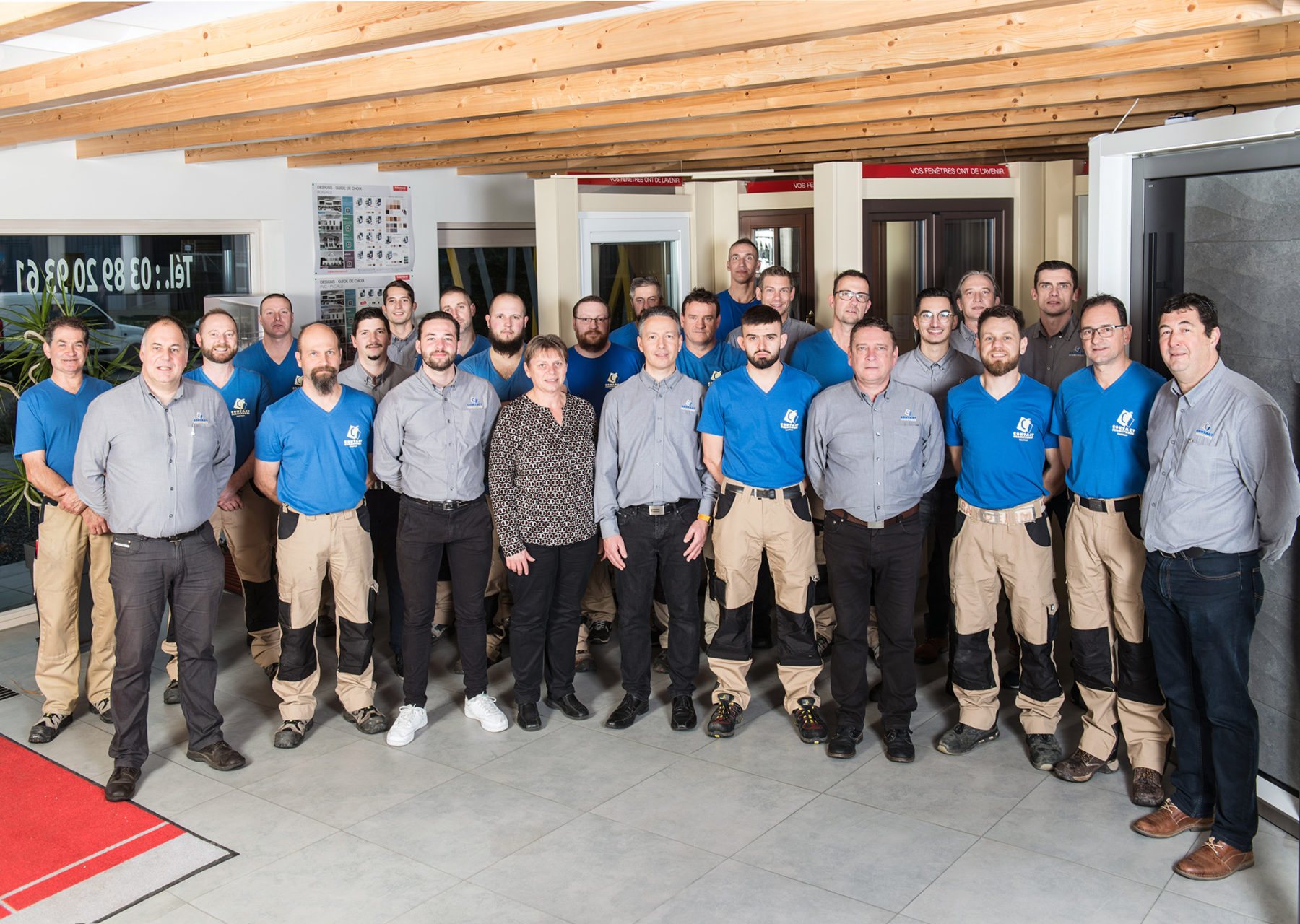 Une vingtaine de membres de l'équipe, en polos bleus ou chemises grises, posent ensemble dans un showroom aux poutres en bois.