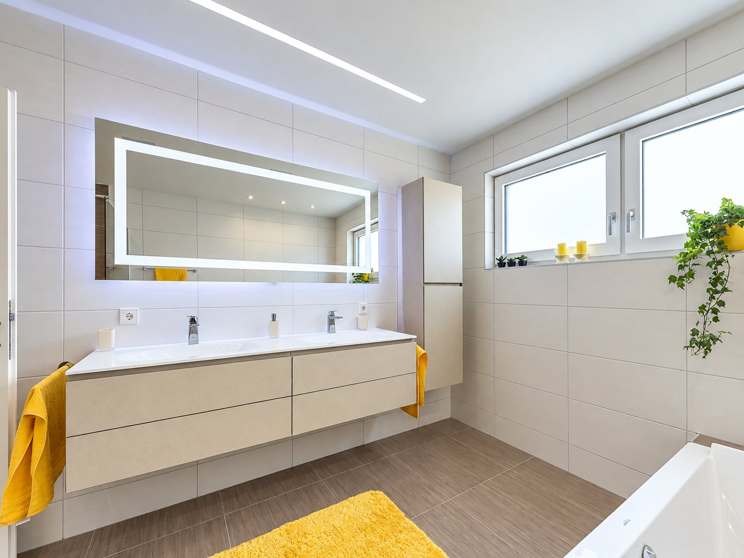 Salle de bain contemporaine aux carreaux clairs avec meuble double vasque suspendu, grand miroir rétroéclairé, serviettes et tapis jaunes.
